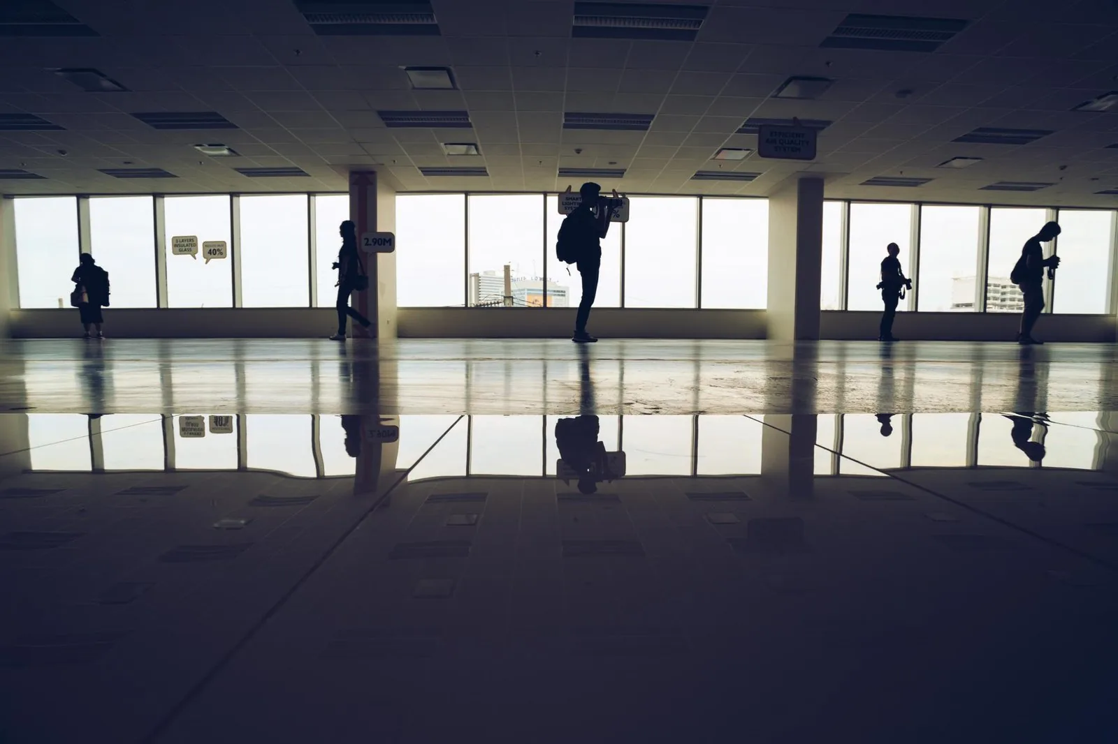 An open-plan office floor at dusk, figures silhouetted against tall windows