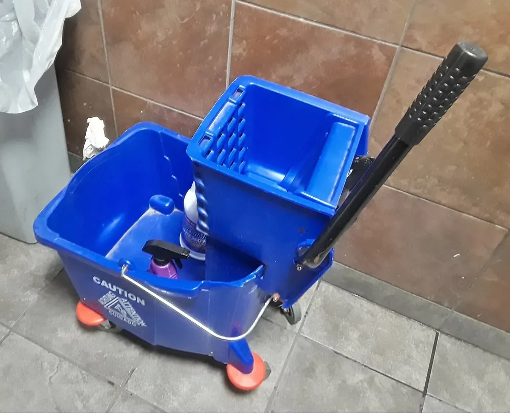 A mop bucket and wringer set down on a tiled floor